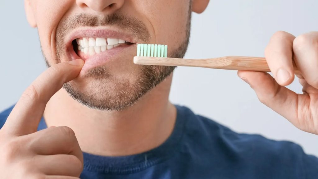 Man Pointing To Gums While Holding Toothbrush