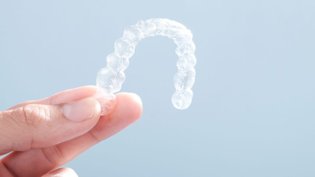 A hand holding a clear Invisalign aligner