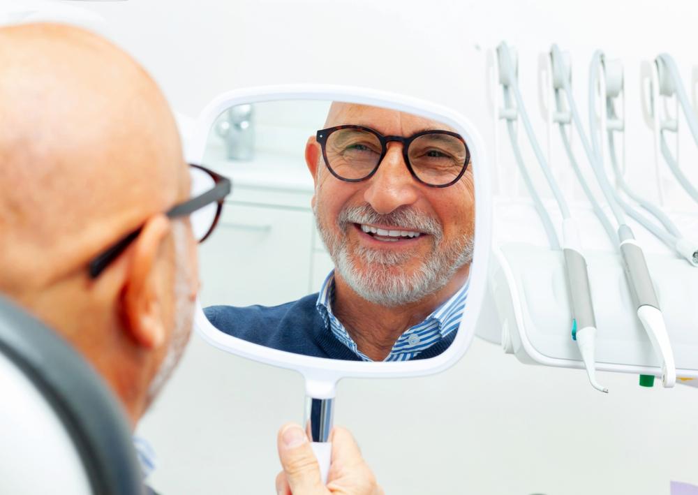 A senior smiles in the mirror at the dentist's office after getting dental implants. What is the dental implant process step by step?