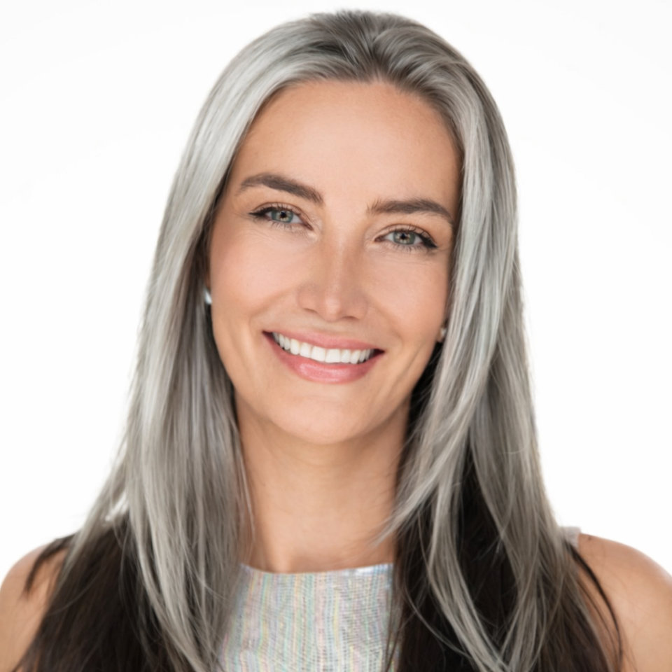 A woman with long straight gray hair and light eyes smiles at the camera against a white background.