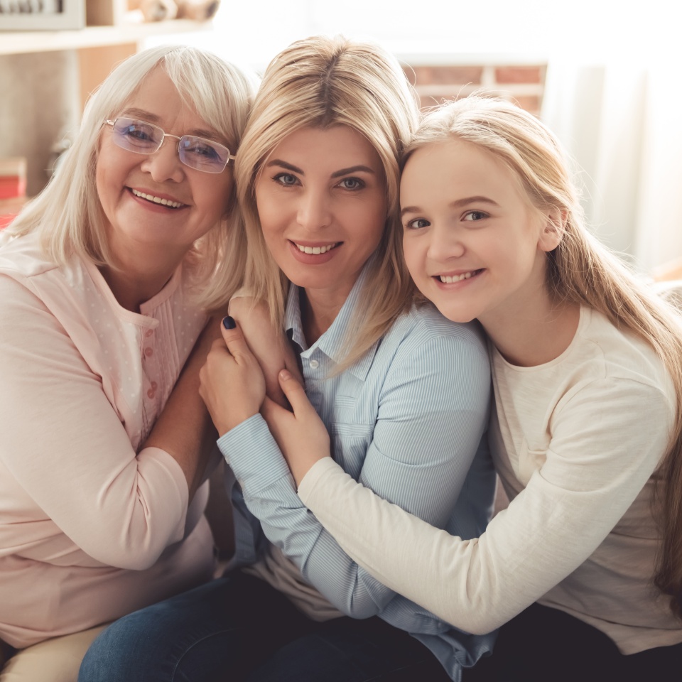 Three generations of women. Beautiful granny mother and daughter are hugging looking at camera and smiling while sitting on couch at home