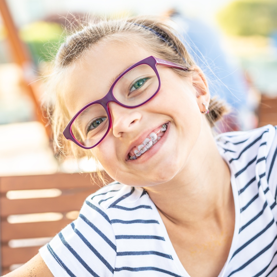 Young preteen girl in glasses wearing braces smiles at the camera on a summer day.