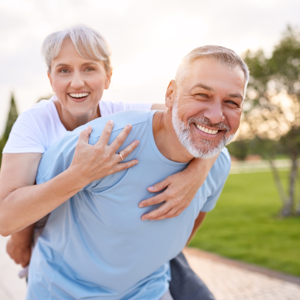 Portrait of lovely happy elderly couple on morning run outside in city park, retirees wife and husband rejoice in active lifestyle, smiling woman tenderly embracing her spouse after routine jogging