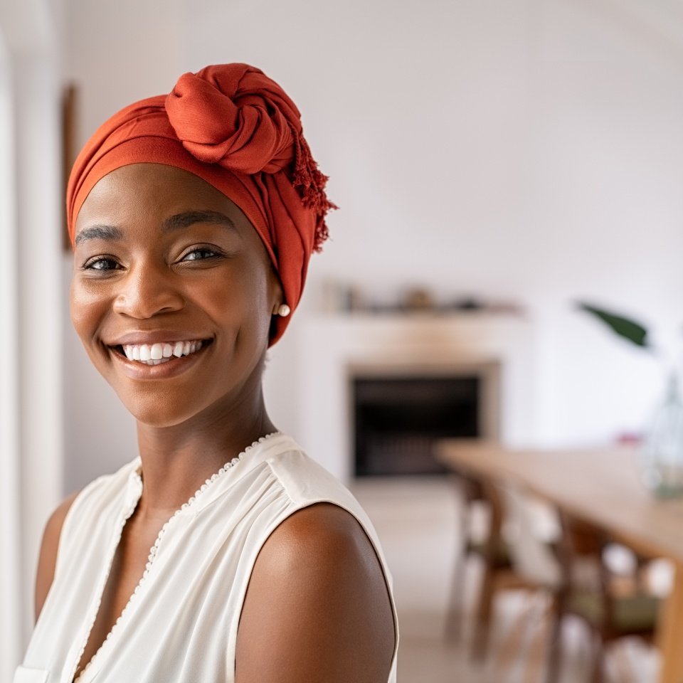 Portrait of a beautiful african woman smiling while looking at camera. Mid adult woman with traditional african headscarf stay at home and smiling. Cheerful mature lady standing near the window.