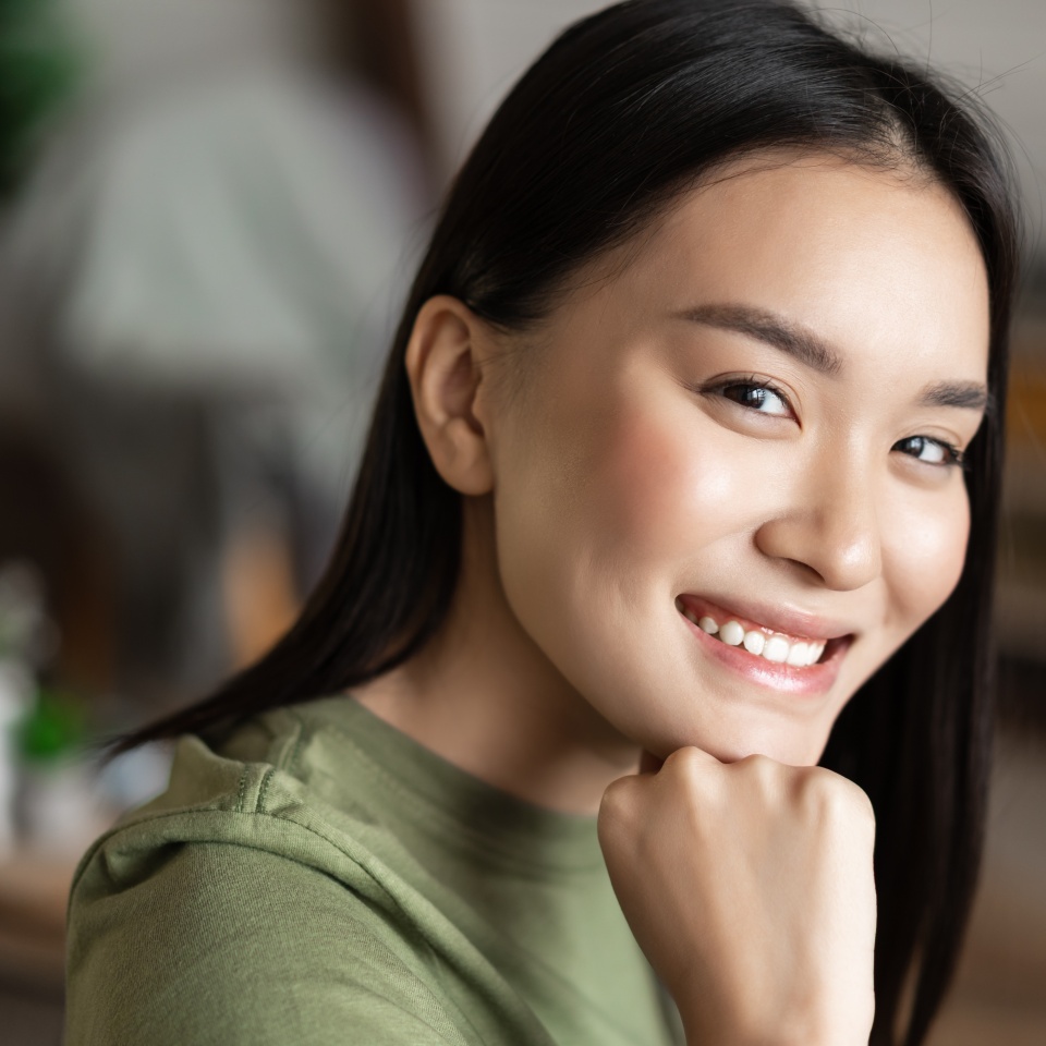 Portrait of young asian woman with clean glowing skin, looking and smiling at camera, sitting at home alone in living room. Lifestyle concept