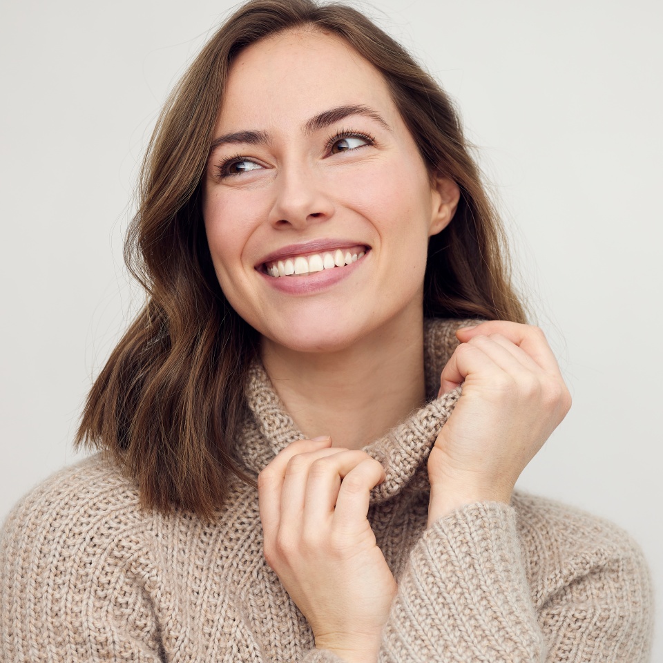Portrait of young happy woman smiling on white background while looking left. Big smile on her face, looking beautiful, natural and charming.