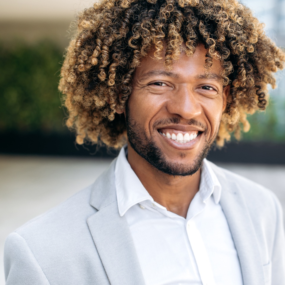 Close-up photo of a proud handsome charismatic confident curly haired brazilian or hispanic man, successful executive, standing outdoors, looking at the camera, smiling friendly