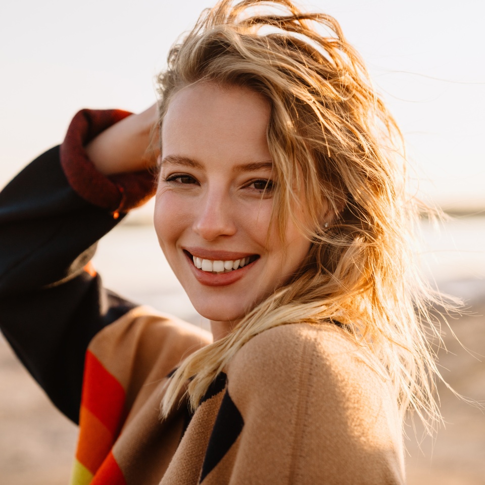 Happy young white woman smiling while walking by seashore on sunny day