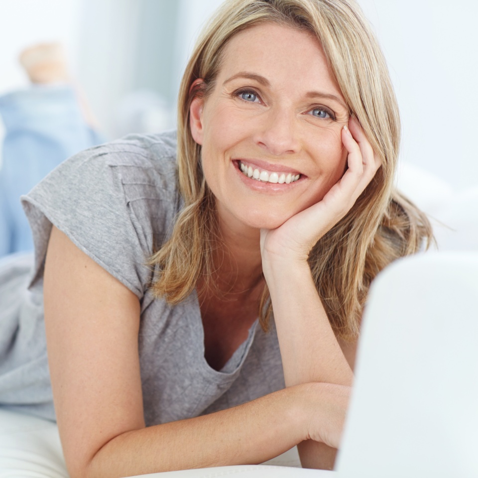 Portrait of mature woman lying on sofa in living room, happiness and relaxing in comfort at home. Smile, lazy weekend time and happy woman in peace chilling on comfortable couch in apartment on break