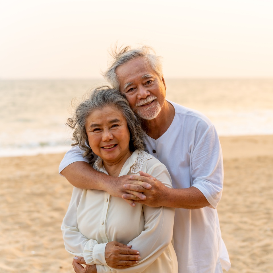Portrait of Happy Asian family senior couple with gray hair walking together at tropical beach at summer sunset. Retired elderly people enjoy outdoor lifestyle travel nature ocean on holiday vacation.