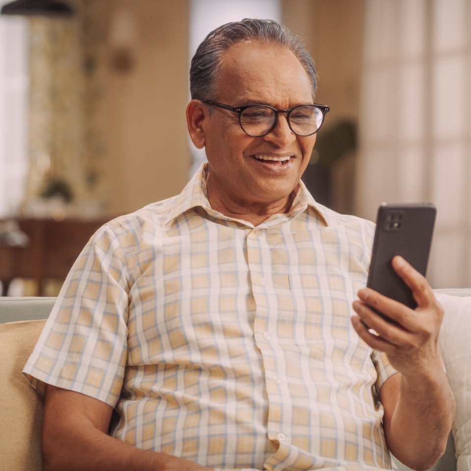 Elderly Indian Man Using Phone for Video Call, Smiling and Happy: Talking with Old Friends and Sharing Life Updates. Cherishing Meaningful Conversations and Laughter with Family Remotely