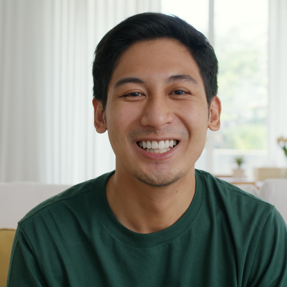 Close-up adult male Gen Z asia people relax look at webcam camera toothy smile sit at home sofa couch. New house owner young latin man guy happy joy cheerful face in urban modern health care lifestyle