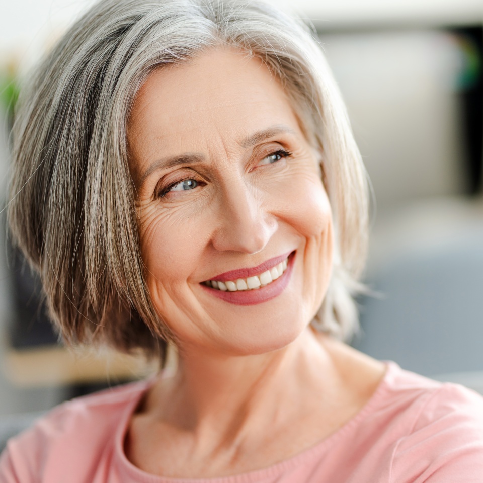 Closeup portrait smiling confident senior woman sitting on comfortable sofa at home. Happy retired female with stylish gray hair, white teeth looking away. Natural beauty, healthy lifestyle concept