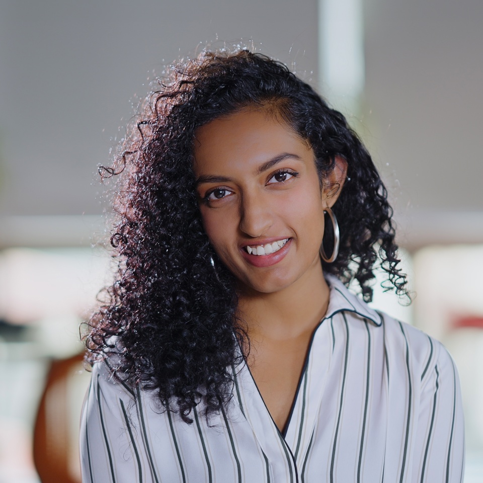 Indian curly hair young adult gen z smiling cute corporate girl standing proud look cam indoor office place. Confident happy business woman worker do pose head shot portrait video at job workplace