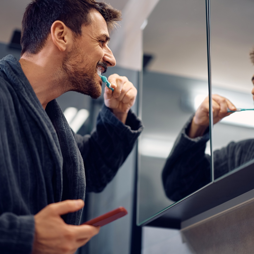 Happy man brushing his teeth while looking himself in am mirror.