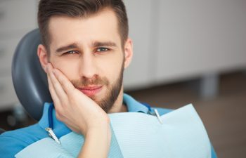 Shot of a young man with tooth pain while sitting in a dentist's chair.