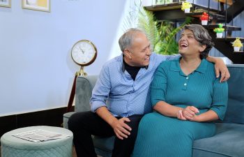 Indian happy middle aged old husband wife sitting on comfy sofa couch making funny communication at indoor home. Smiling older senior couple enjoying romantic talking together summer vacation holiday