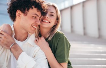 Smiling beautiful woman and her handsome boyfriend. Couple in casual summer clothes. Happy cheerful family. Female and man having fun. They posing in the street in sunny day. Sit at stairs