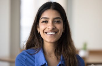 Head shot of beautiful young Indian woman sitting alone on sofa at home, posing for camera exude optimism, positive mood. Generation Z female, profile picture, portrait of virtual meeting participant