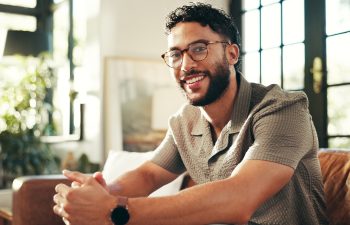 Portrait, glasses and happy man relax in home on sofa for peace, calm and break on staycation with confidence. Face, smile and person in living room for chill, rest and comfort in apartment in India