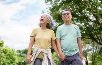 Glasses old man smiling and holding hand with old woman while walking together after exercise in park. Elderly couple, Green Nature, Chilling Outdoor.