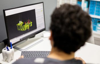 An unrecognizable dentist shows an implant surgery plan on his office monitor through a 3D X-ray. 3D implantology concept.